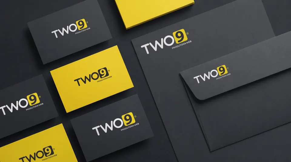 Cartões de visita em carvão e em amarelo, papel timbrado e envelope da Two9 sobre uma mesa escura.